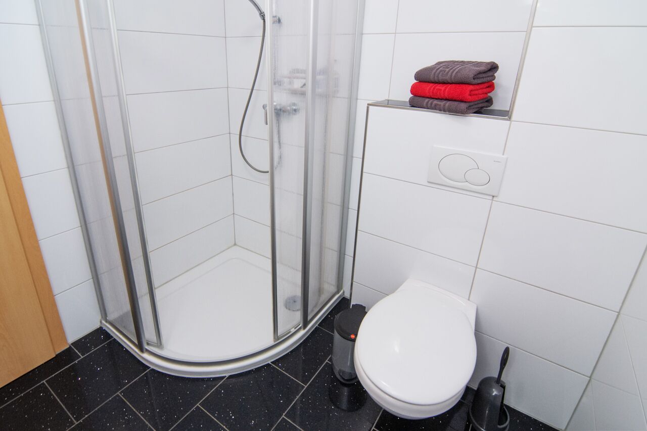 Un baño con ducha de vidrio, un inodoro blanco y un perchero con toallas dobladas.