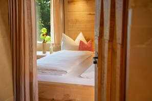 Ein Schlafzimmer mit hölzernem Kopfteil, weißer Bettwäsche und einer Vase mit Blumen am Fensterbrett.