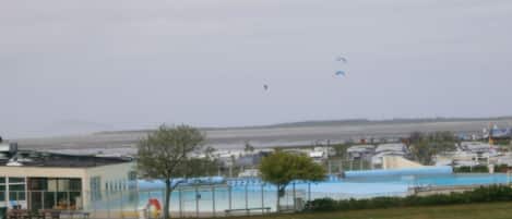 A view of a park with a swimming pool, a building with a glass facade, and a distant shoreline.