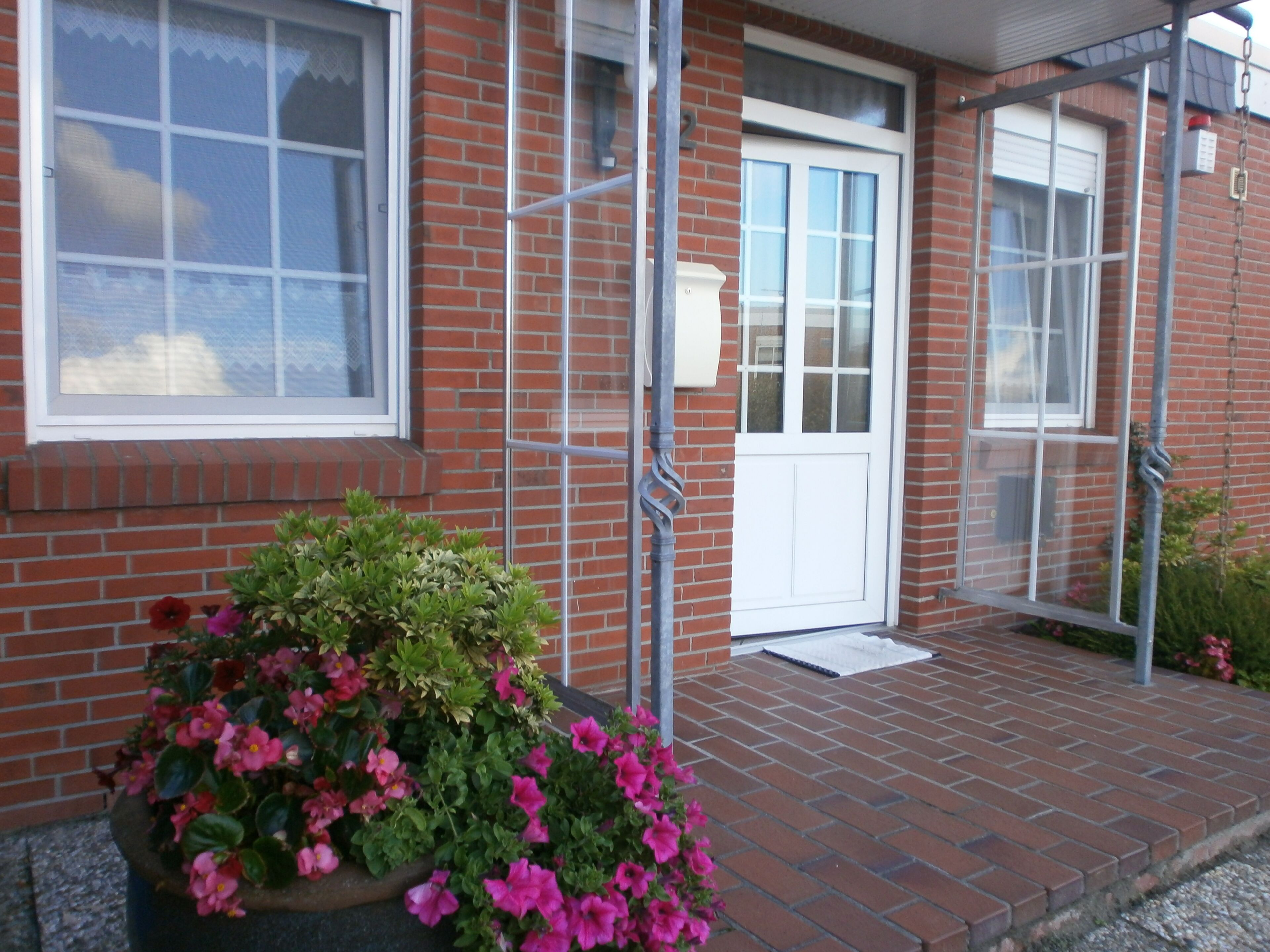A brick building with a white door and windows, a metal railing, and a flower planter on the porch.