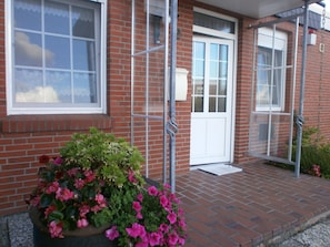 A brick building with a white door and windows, a metal railing, and a flower planter on the porch. - Comfortable vacation home near the beach  (Dornumersiel)