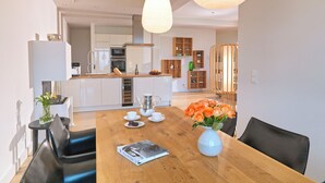 Una cocina moderna con armarios blancos, una isla central y una zona de comedor con una mesa y sillas de madera.