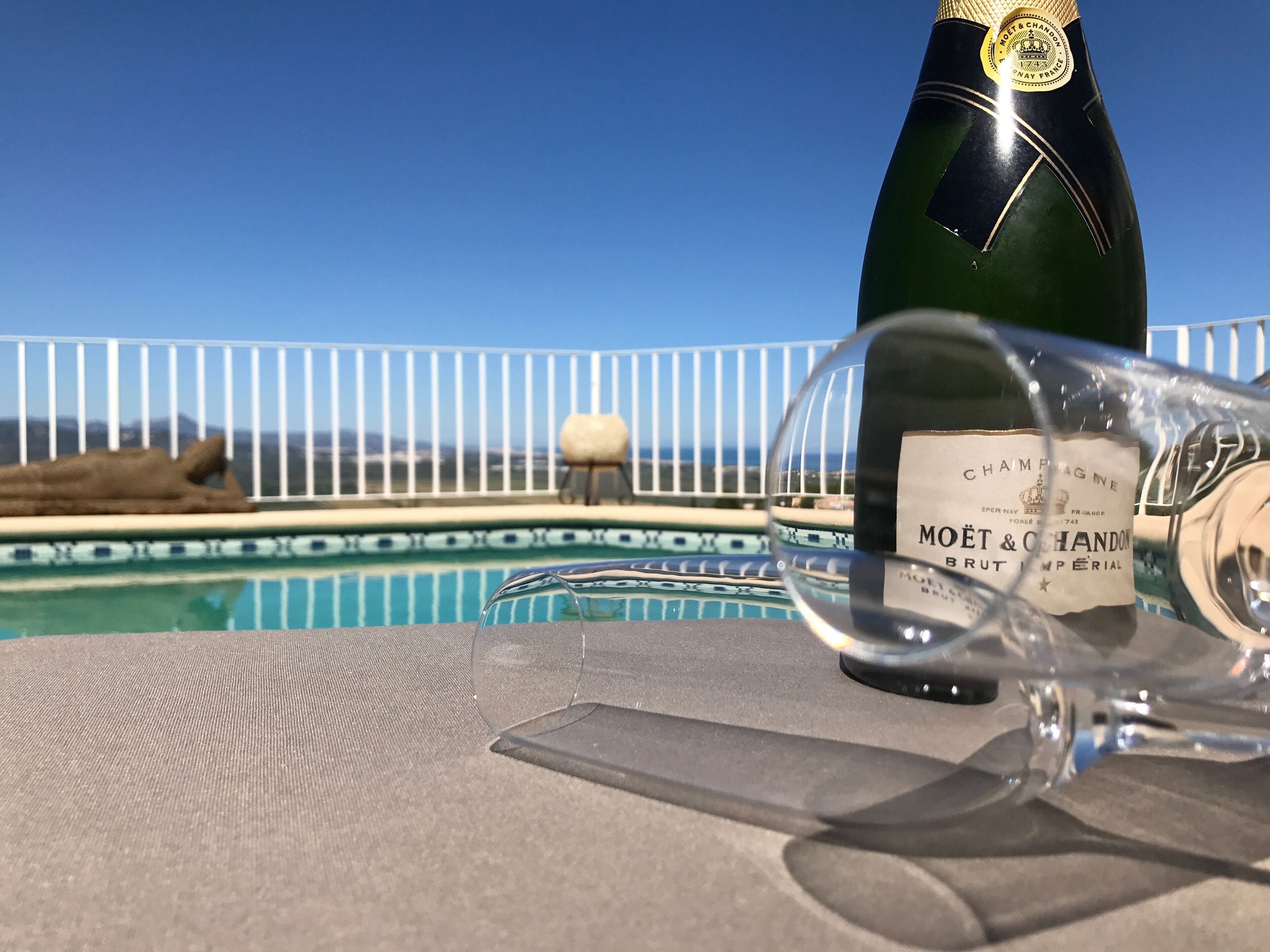 Une bouteille de champagne Moët & Chandon Brut à côté d’un verre, sur une terrasse au bord de la piscine, avec vue sur la mer.