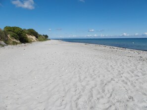 En bred, sandstrand med milda vågor och en klarblå himmel.