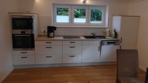 Une cuisine compacte dotée d’appareils électroménagers intégrés, d’une fenêtre avec stores et d’un plancher en bois.
