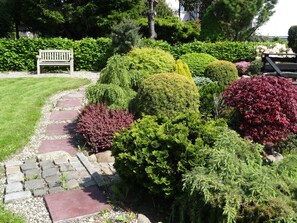 Stroll through the serene garden, surrounded by neatly trimmed shrubs and trees, along a winding stone pathway.