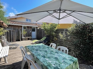 Une terrasse avec une table et des chaises, une plateforme en bois et un grand parasol pour faire de l’ombre.