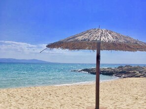 A beach with a thatched umbrella, clear blue sky, and calm sea. - Sunlit, newly renovated apartment with 20sqm balcony and sea view  (Kavala)