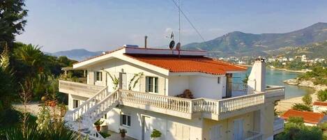 A two-story house with a balcony, a stone staircase, and a view of a lake and mountains.