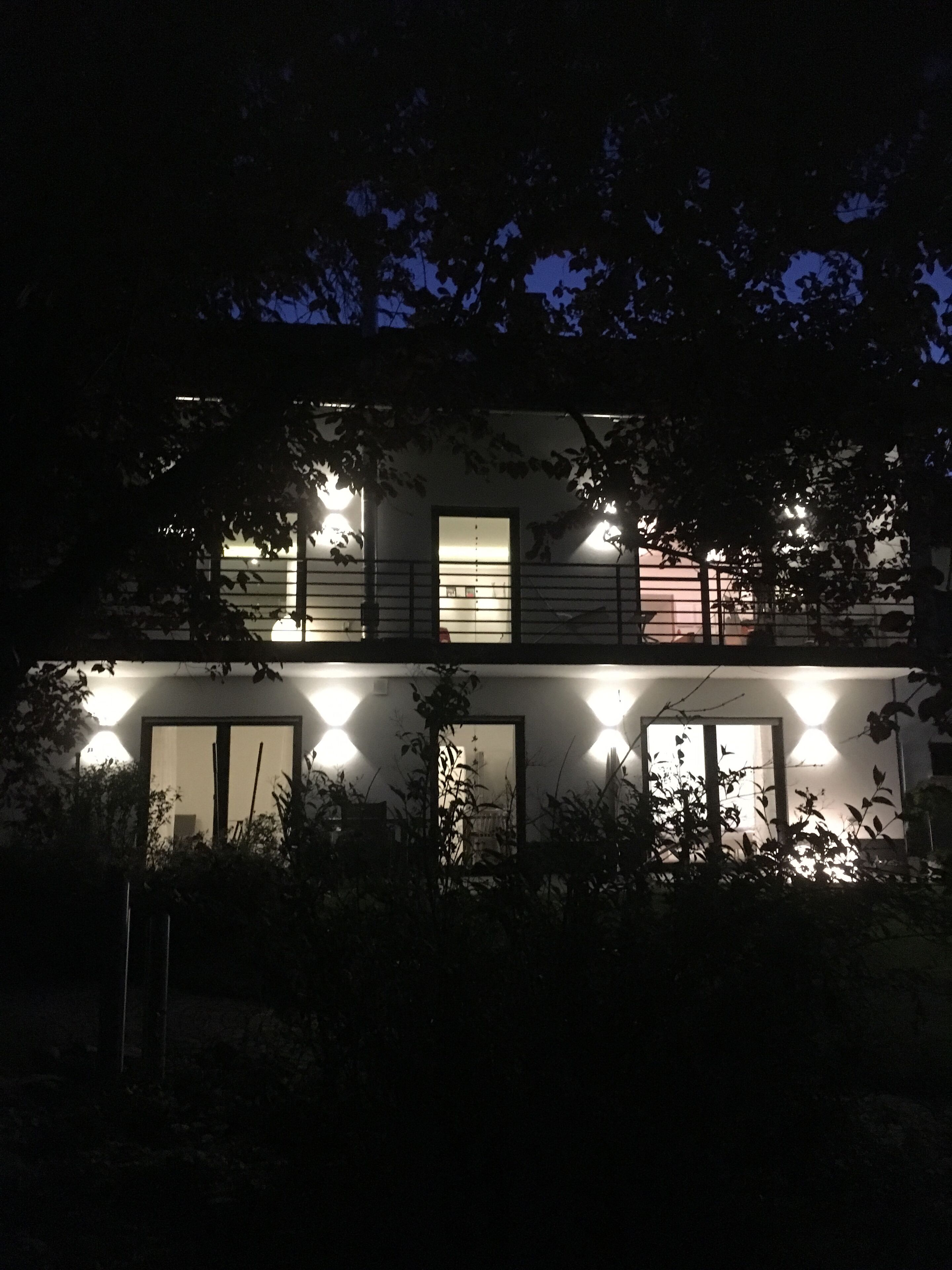 Un edificio de dos pisos con varias ventanas y puertas iluminadas, rodeado de follaje.