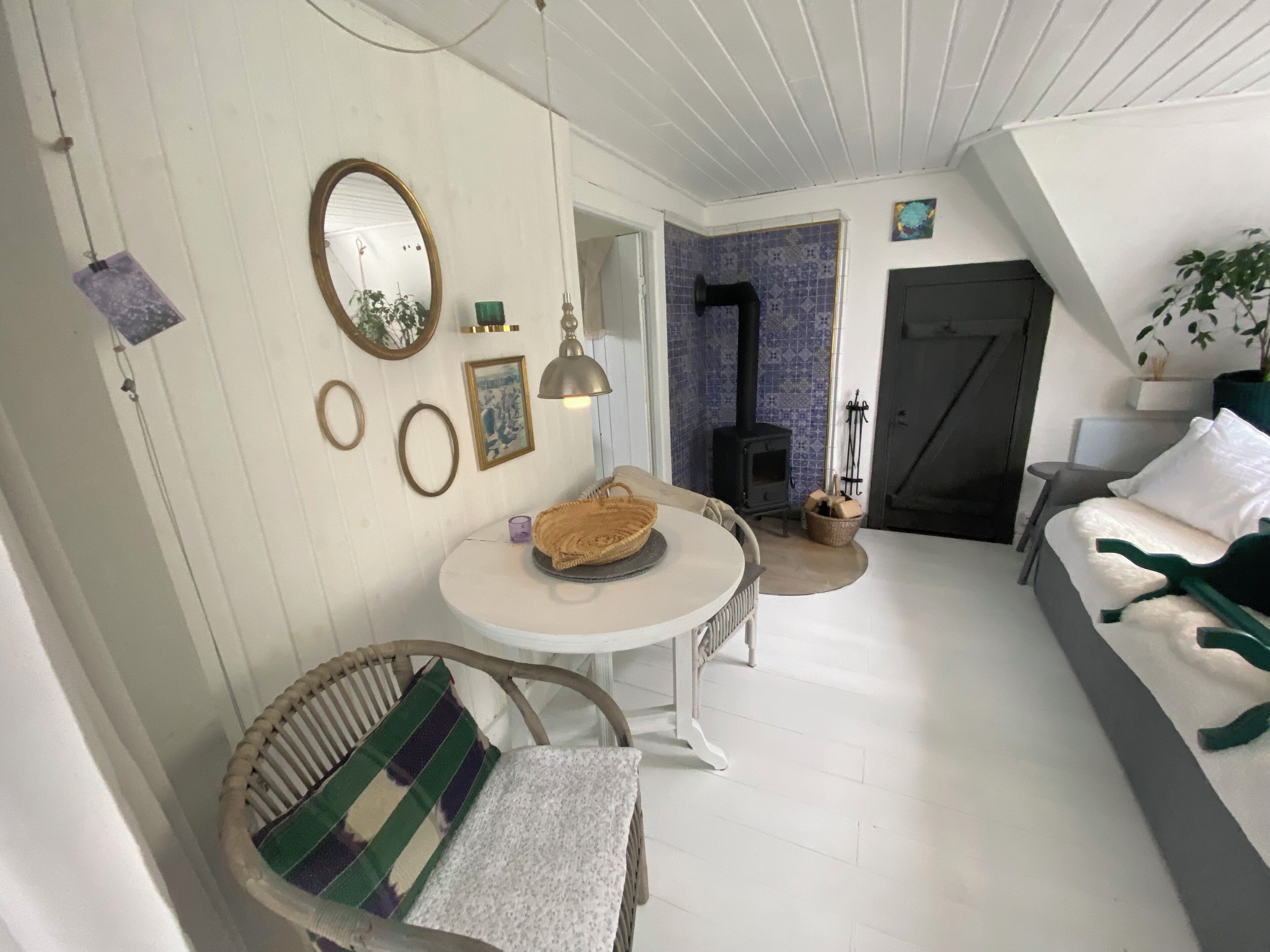 A cozy living room with a round table, a wicker chair, a sofa, a fireplace, and a door leading to another room.