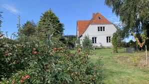 Ein Haus mit rotem Ziegeldach, umgeben von einem gepflegten Garten mit Apfelbäumen.