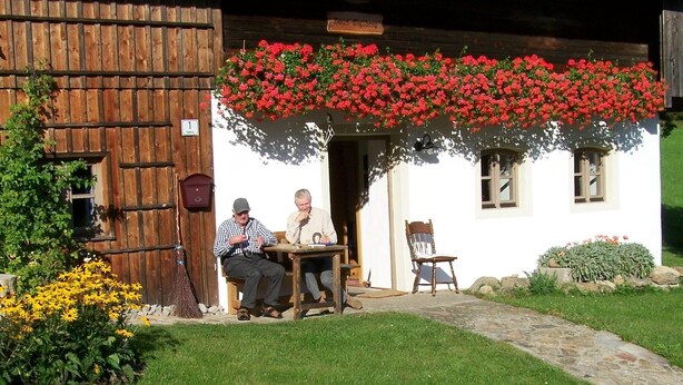 A rustic building with a wooden exterior, a porch with two wooden chairs, and a hanging flower basket. - secluded, 300 year old landmarked Holiday Home, renovated (Bayern)