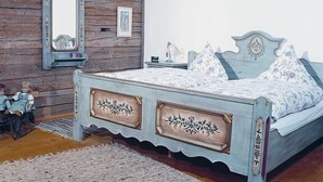 A bedroom with a wooden wall, a bed with floral bedding, a dresser, and a mirror. - secluded, 300 year old landmarked Holiday Home, renovated (Bayern)