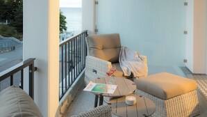 A balcony with wicker furniture, a table with a candle, and a magazine. - Summerbreeze Cloud Luxury Apartment with Ocean View | Skypool, Sauna & Beach Chair | Dog-Friendly (Sellin)