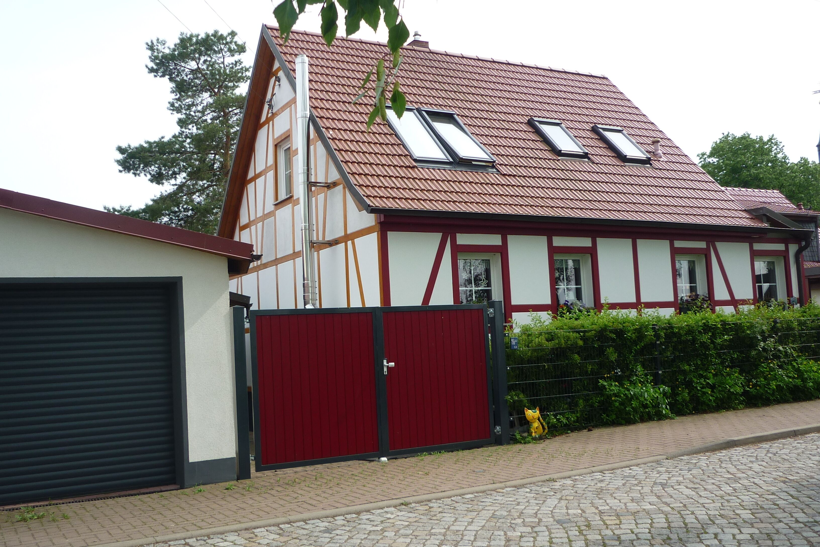 A traditional half-timbered house with a red roof, two skylights, and a red gate.