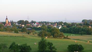 Un paysage rural avec des maisons, un clocher d’église et des bottes de foin dans un champ.