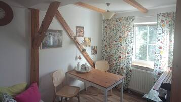 Une pièce chaleureuse avec une table en bois, un canapé agrémenté de coussins à motifs floraux, une fenêtre avec des rideaux et un radiateur.