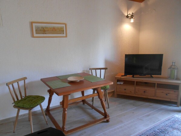 A dining area with a wooden table, two chairs, a television on a stand, and a small cabinet. - romantic cottage for 2 persons (Rovinsko Selo)