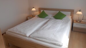 Un letto rifatto con lenzuola bianche e cuscini verdi, due abat-jour e un quadro appeso al muro.
