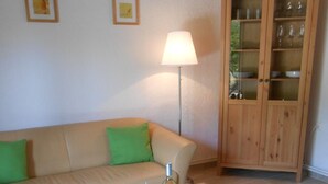 Un soggiorno con un tavolino in legno, un divano con cuscini verdi, una lampada da terra e un mobile contenitore in legno con ante in vetro.