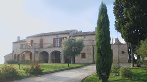Un bâtiment historique en pierre, doté d’une cour intérieure, de portes en arc de cercle et d’un chemin de gravier menant à l’entrée.