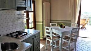 Une cuisine équipée d’une cuisinière à gaz, d’un évier et de meubles blancs. On y trouve une table à manger avec des chaises et un saladier rempli de fruits.