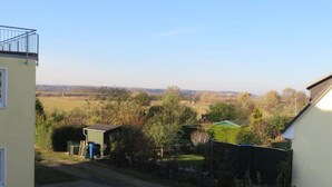 A residential area with a paved driveway, a green-roofed shed, and a view of a distant field. - Stylish 3 rows App. up to 4 people + Toddler + wifi, 250 m to the Baltic Sea (Börgerend)