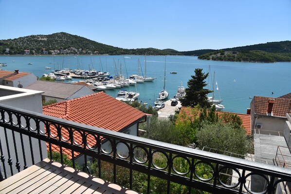 A marina with boats docked, surrounded by buildings with red-tiled roofs, and a hill in the background.