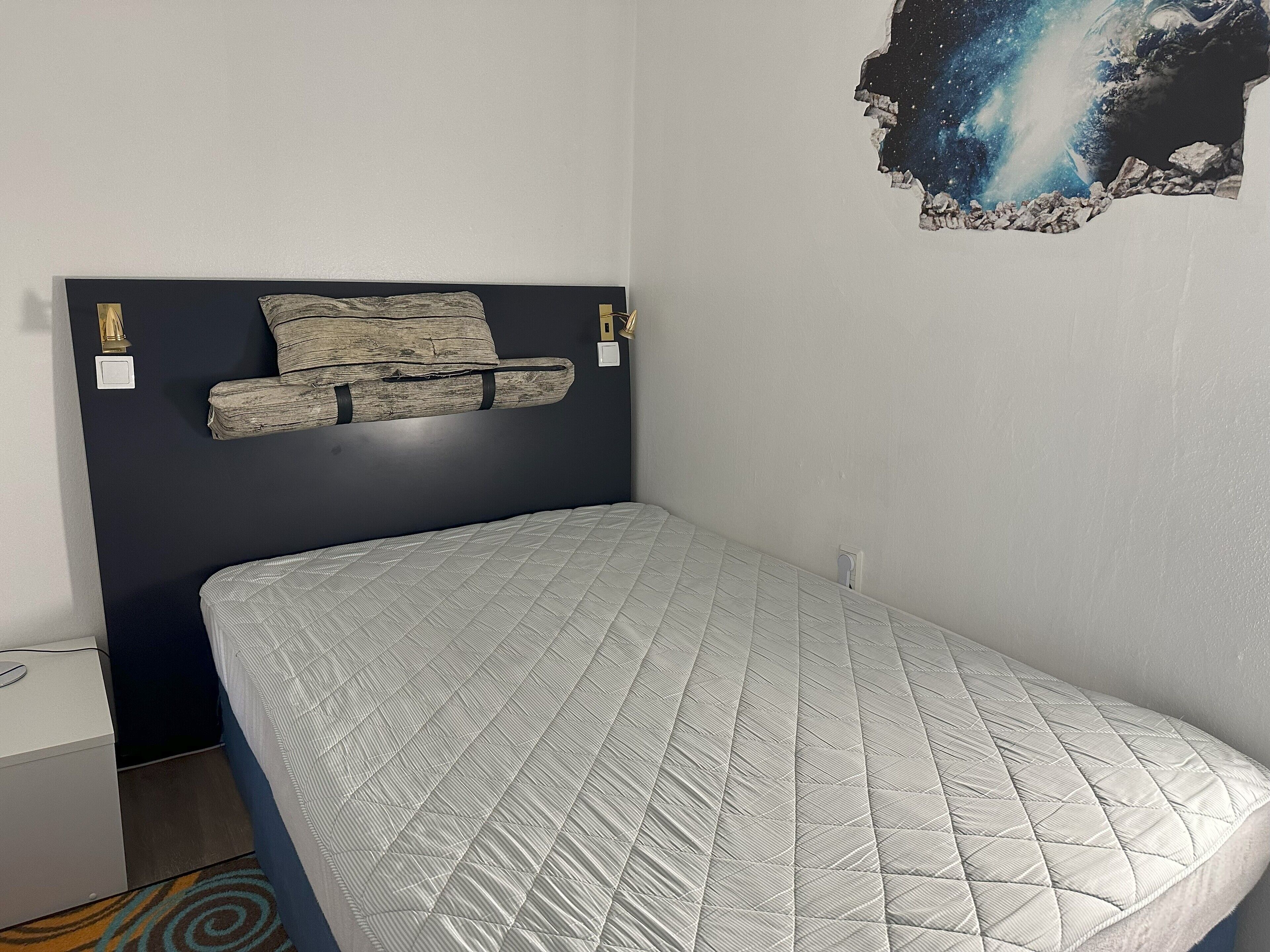 Une chambre à coucher comprenant un lit, une tête de lit, une table de chevet et un élément décoratif mural.