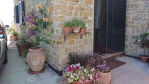 A stone building with a door and windows, potted plants, and a car parked outside. - Apartment with a beautiful panoramic terrace on the Cilento coast (Ogliastro Cilento)