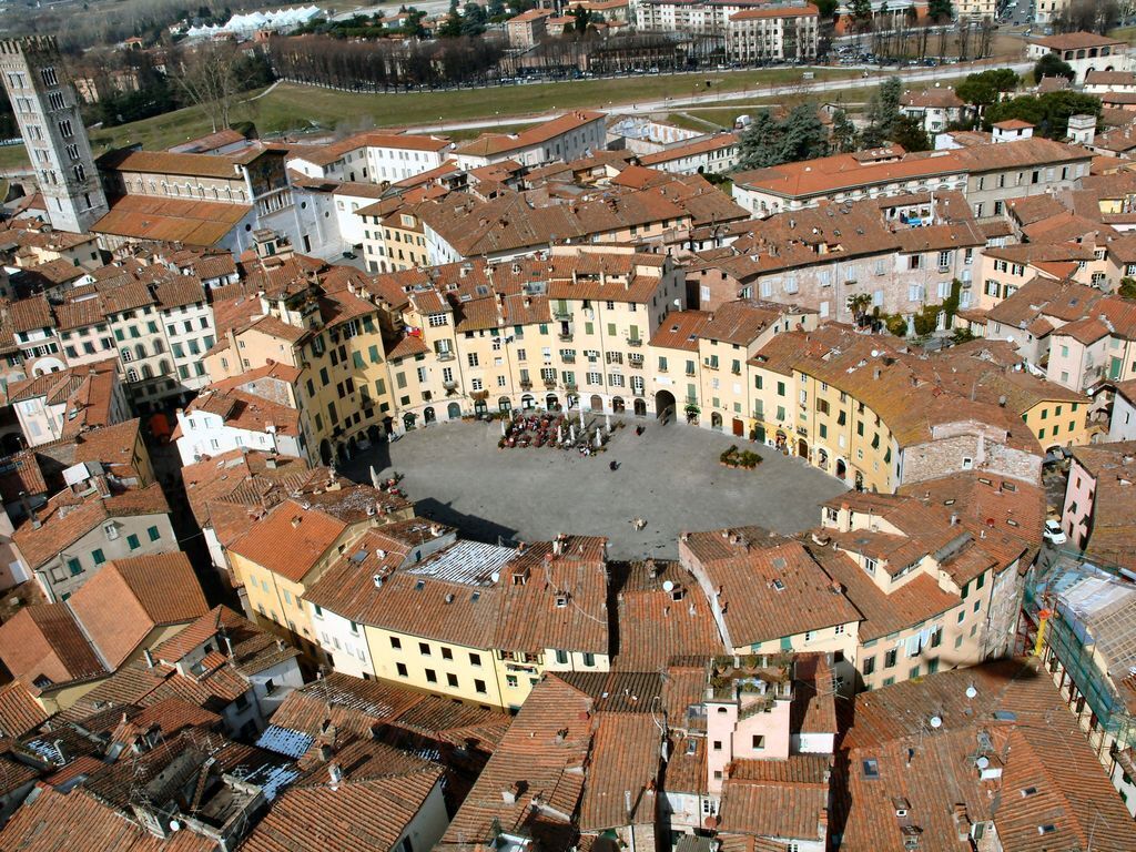 A historic square surrounded by buildings with red-tiled roofs and a prominent tower.
