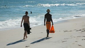 Twee mensen lopen over een zandstrand, met golven in de verte.