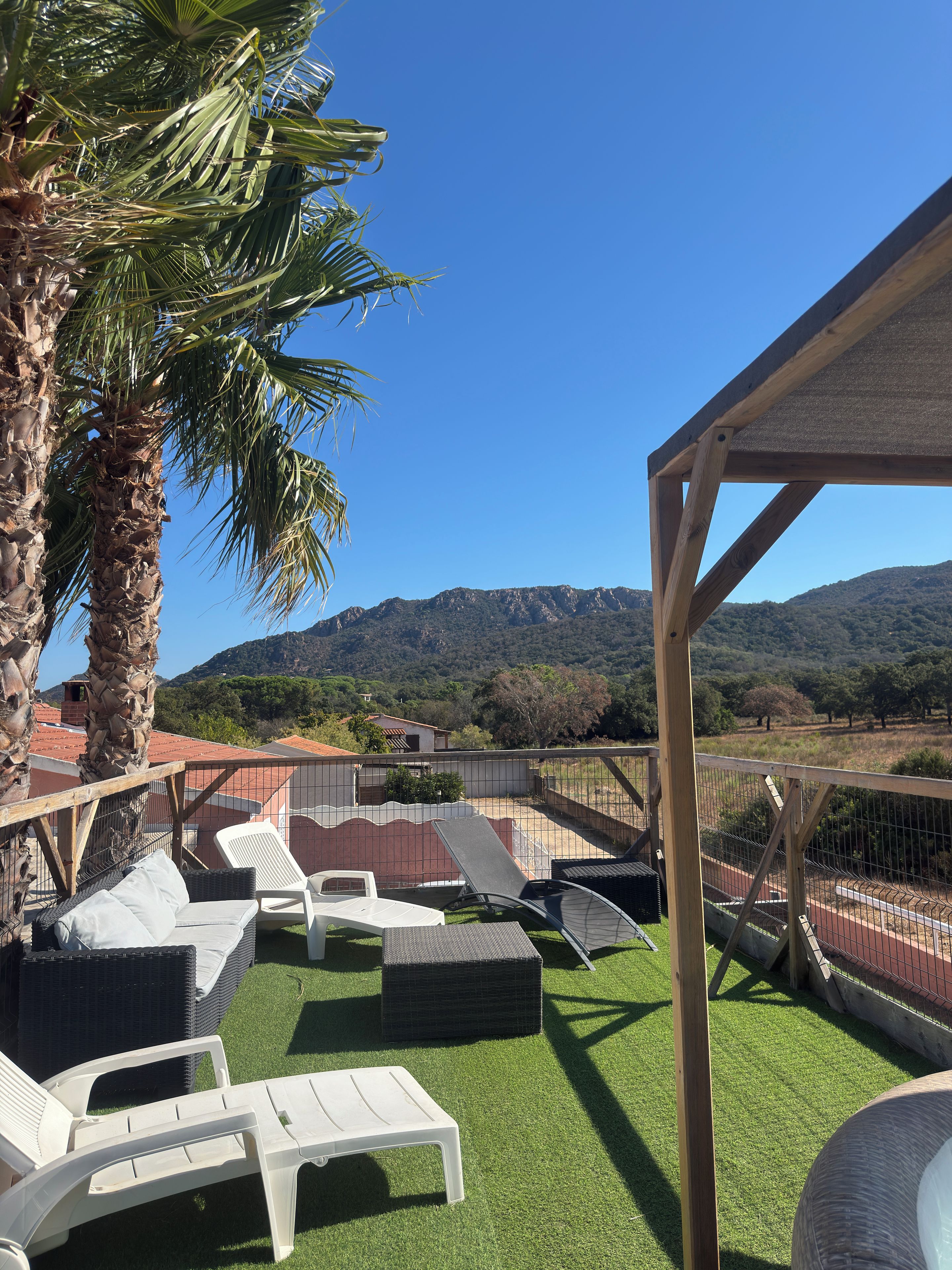 A patio area with white lounge chairs and a pergola structure, overlooking a mountainous landscape.