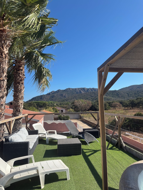 A patio area with white lounge chairs and a pergola structure, overlooking a mountainous landscape.
