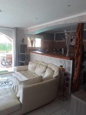 Una sala de estar con un sofá color crema, una mesa de centro y una zona de cocina con mostrador y armarios.