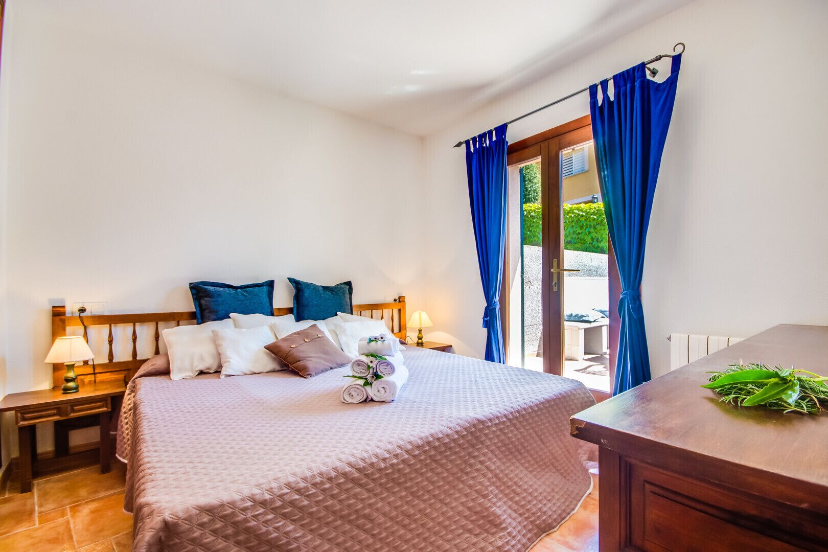A hotel room with a bed, pillows, a nightstand with a lamp, a wooden headboard, and a view through a glass door.
