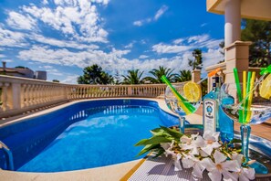 A pool with clear blue water, surrounded by a white balustrade, with a table in the foreground holding a bottle of Bombay Sapphire Gin, a glass with a lemon slice and green straw, and white flowers. - House with pool in Alcudia Ronda near the beach (Alcanada)