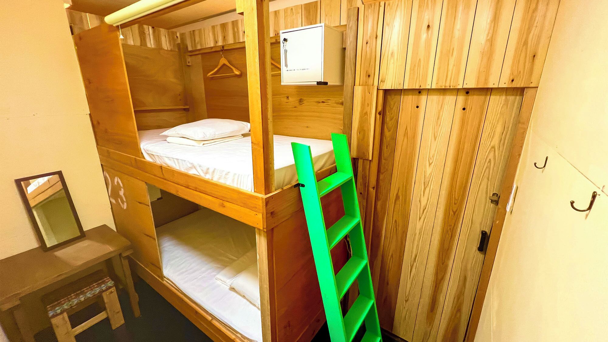 Habitación con literas, una escalera verde, una mesita pequeña y un televisor en la pared.