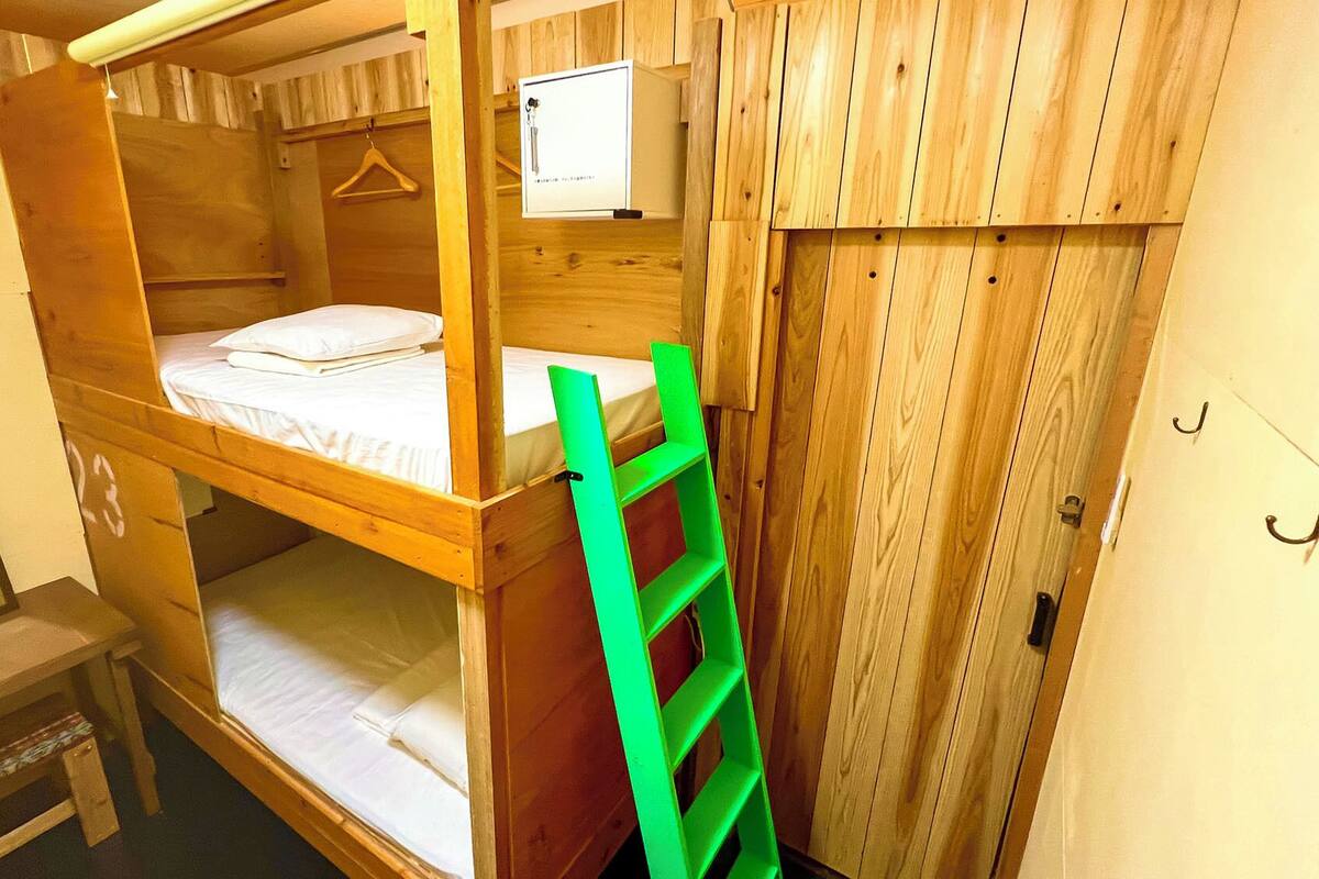 Une chambre avec un lit superposé, une échelle verte, une petite table et un téléviseur fixé au mur.