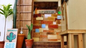 Een houten ingang met een bord waarop 'OPUNTIA' staat en een cactussplant.