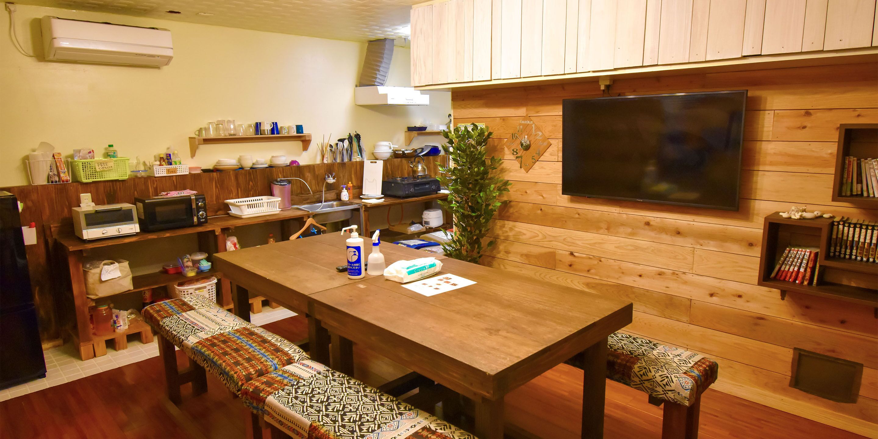 Una cocina acogedora con armarios de madera, un televisor grande y una mesa de comedor con bancos.
