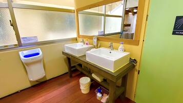 A women's restroom with two sinks, a mirror, a hand dryer, and a trash bin.