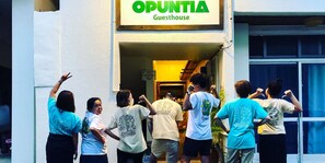 Een groep mensen betreedt een gebouw met een bord waarop staat: OPUNTIA Guesthouse.