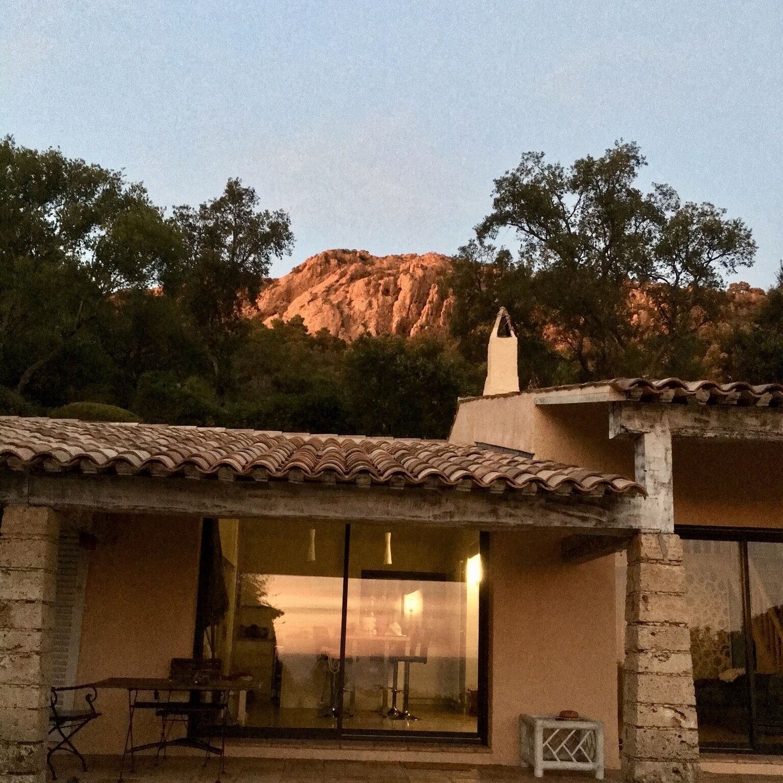 Un edificio de piedra con tejado de tejas, grandes puertas de cristal y una pequeña zona de estar al aire libre.