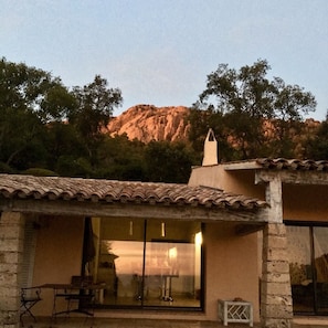 Un edificio de piedra con tejado de tejas, grandes puertas de cristal y una pequeña zona de estar al aire libre.