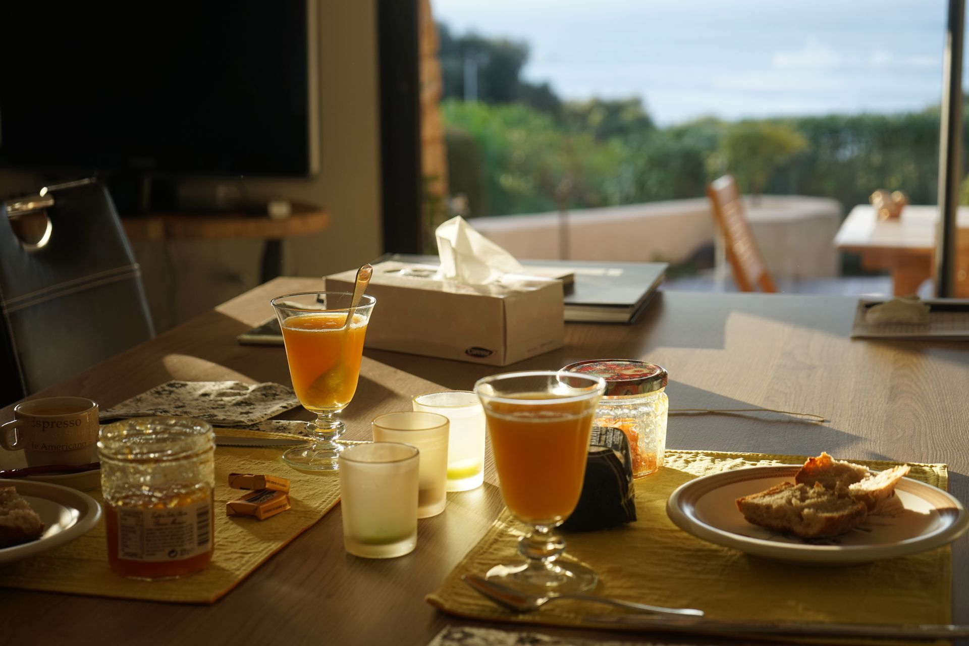 Ein Esstisch mit verschiedenen Gegenständen, darunter ein Glas Orangensaft, eine Kerze, ein Einmachglas und ein Teller mit Brot.