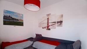 Ein Zimmer mit einem Bett, einem rot-grauen Sofa und einer Wand mit drei Bildern.
