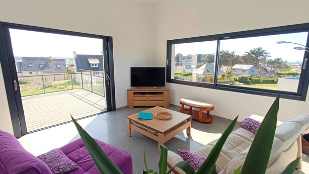 Een moderne woonkamer met een balkon, een televisie, een houten salontafel en twee banken.