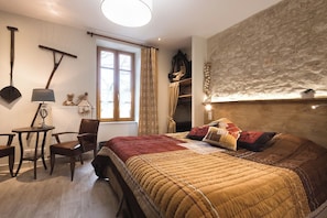 Ein Schlafzimmer mit einem Bett, einem Sessel, einem Schreibtisch, einem Fenster und einer Steinwand.